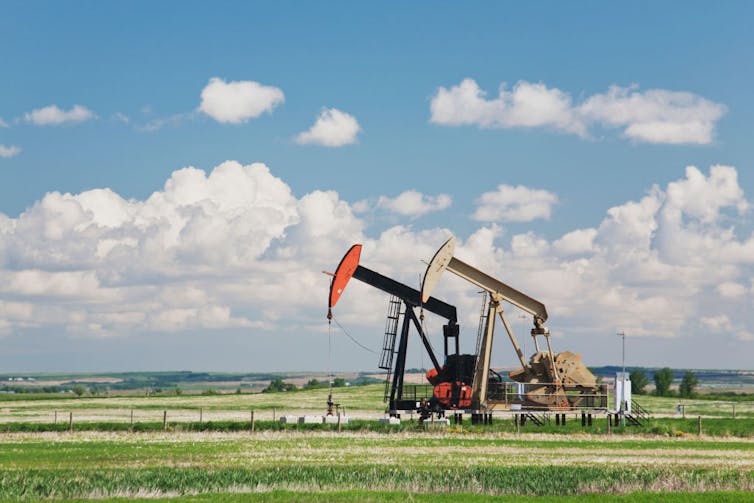 Two huge machines that look like hammers stand in a field under a blue sky with clouds.