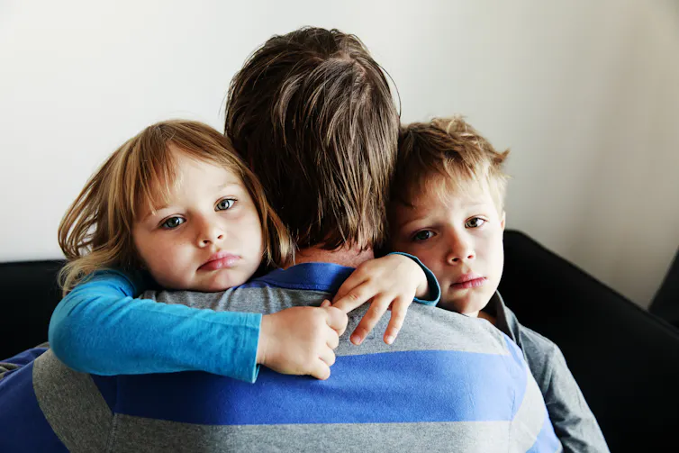 Two sad children seen with a man with his back to the camera