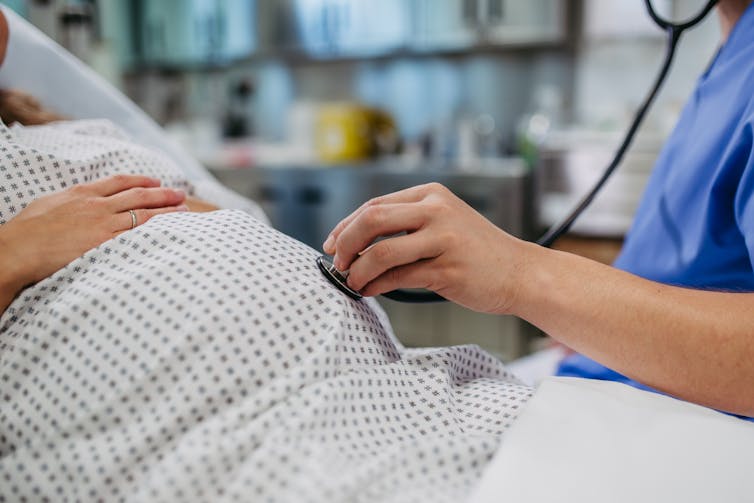 Doctor holding stethoscope on belly of pregnant person