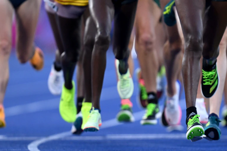 Diversas pernas de atletas numa pista de corrida durante a final feminina dos 10.000 m nos Jogos da Commonwealth de 2022