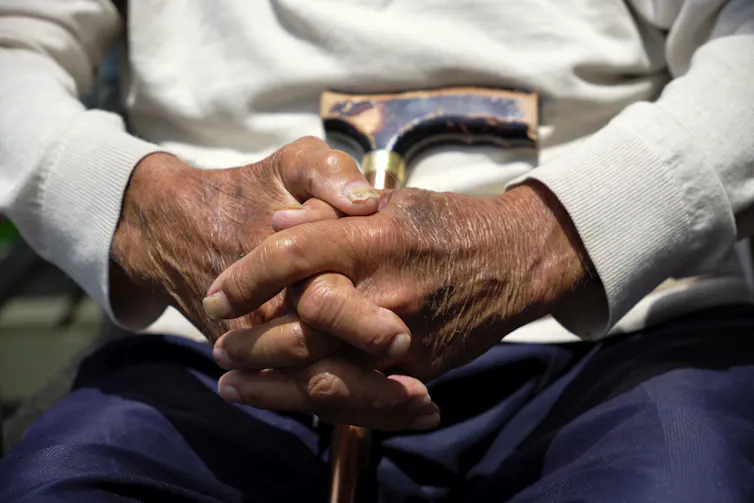 Close-up of a man's clasped hands, with a walking stick