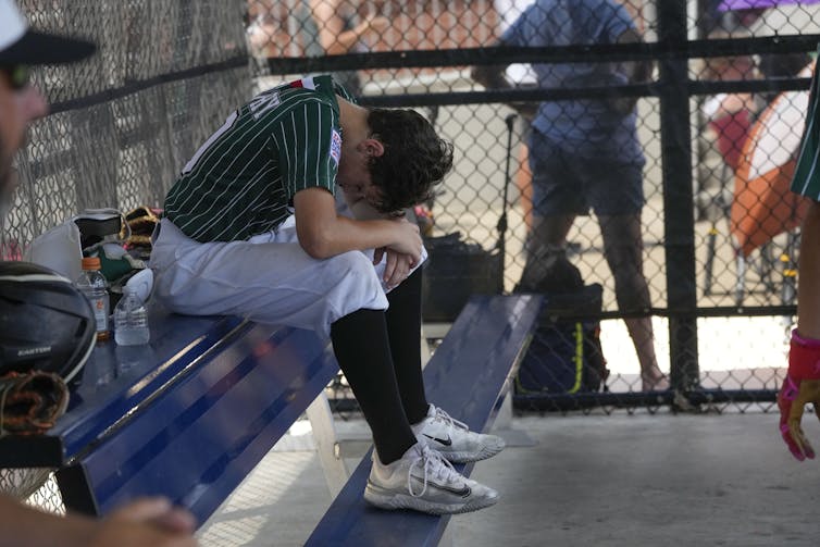 A young baseball player lands head down in the dugout while sitting on a bench.