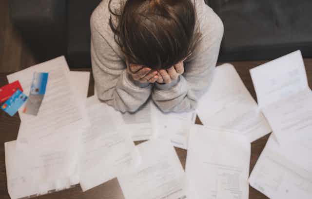 Woman holding head in hands surrounded by paperwork