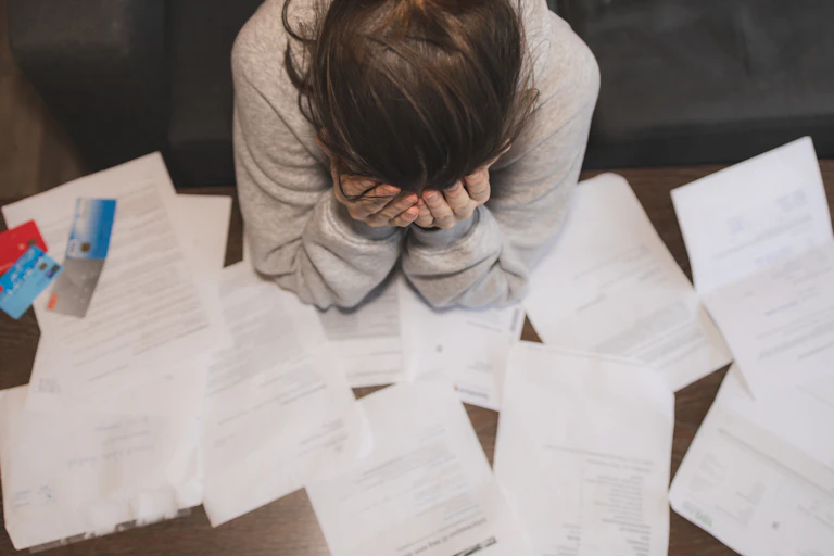 Woman holding head in hands surrounded by paperwork