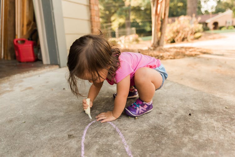 Toddler draws on driveway in chalk