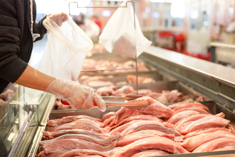 A gloved hand selects cuts of meat from behind a counter.