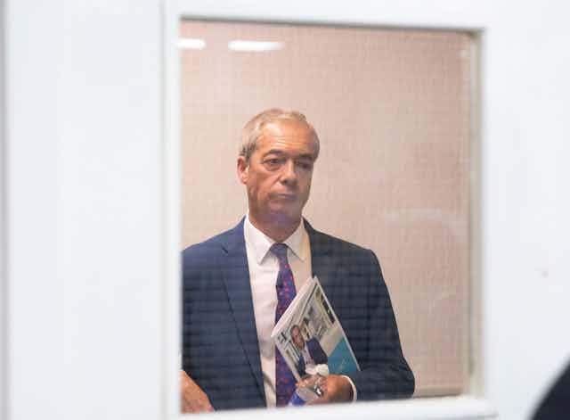 Nigel Farage looking through a glass door. 