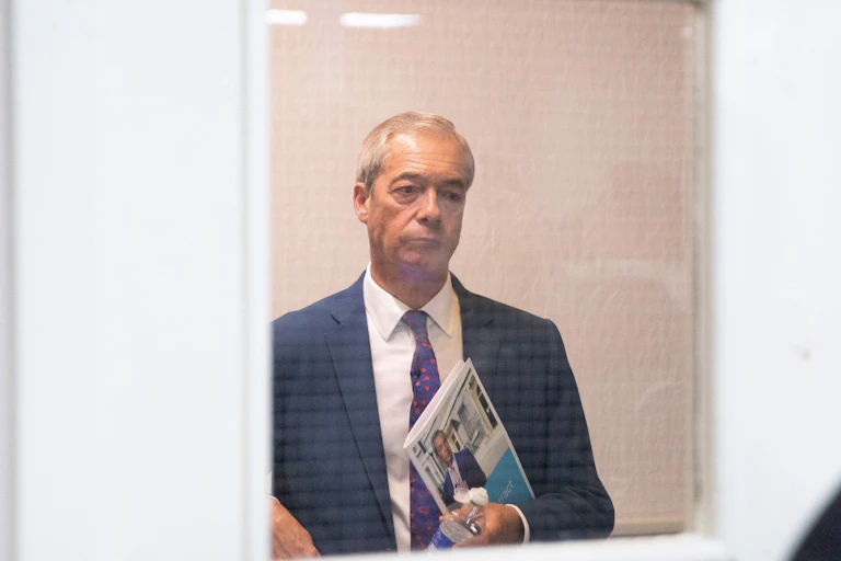 Nigel Farage looking through a glass door.