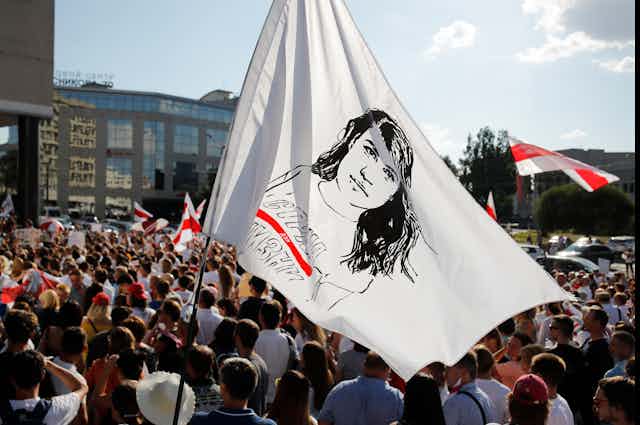 People hold a flag with a sketch of a woman's face amid a large rally.