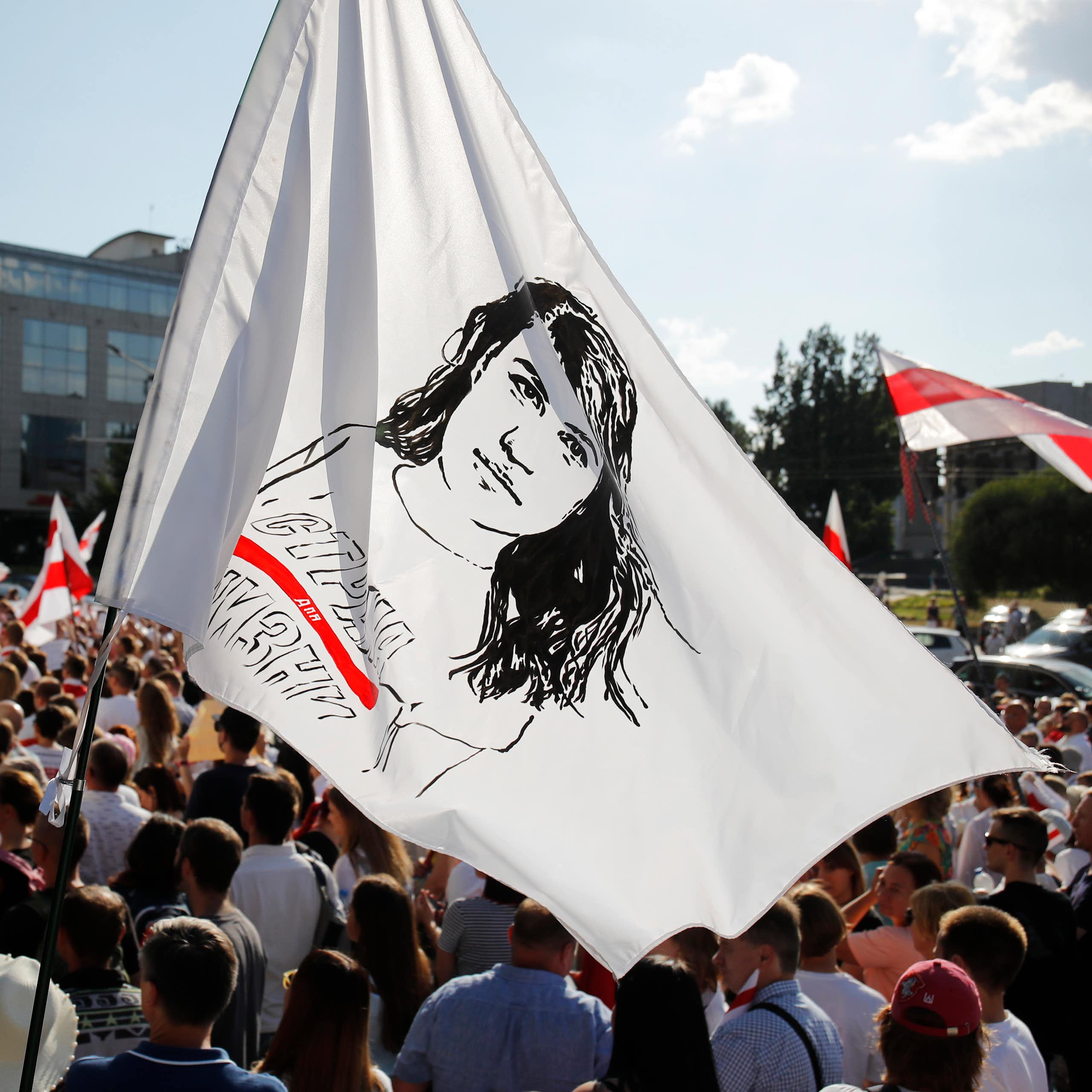 People hold a flag with a sketch of a woman's face amid a large rally.