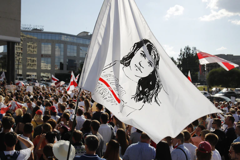People hold a flag with a sketch of a woman's face amid a large rally.