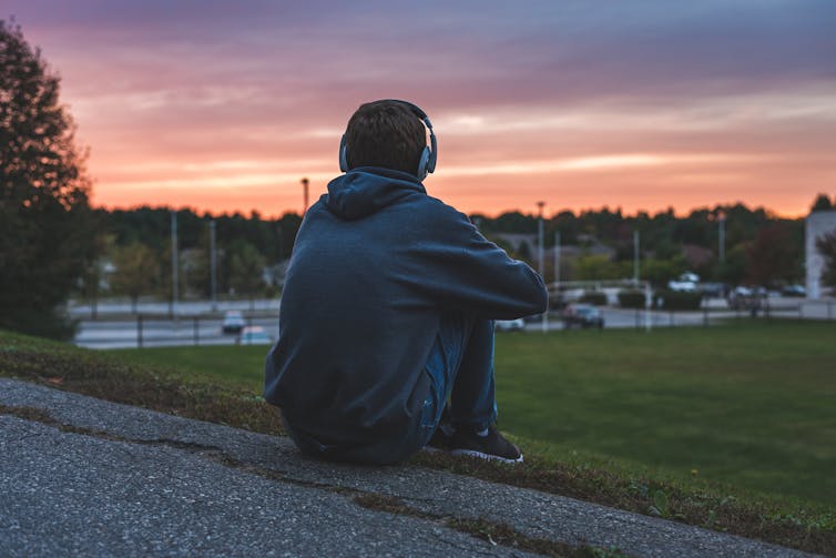 Lone teenager listens to music on a hill.
