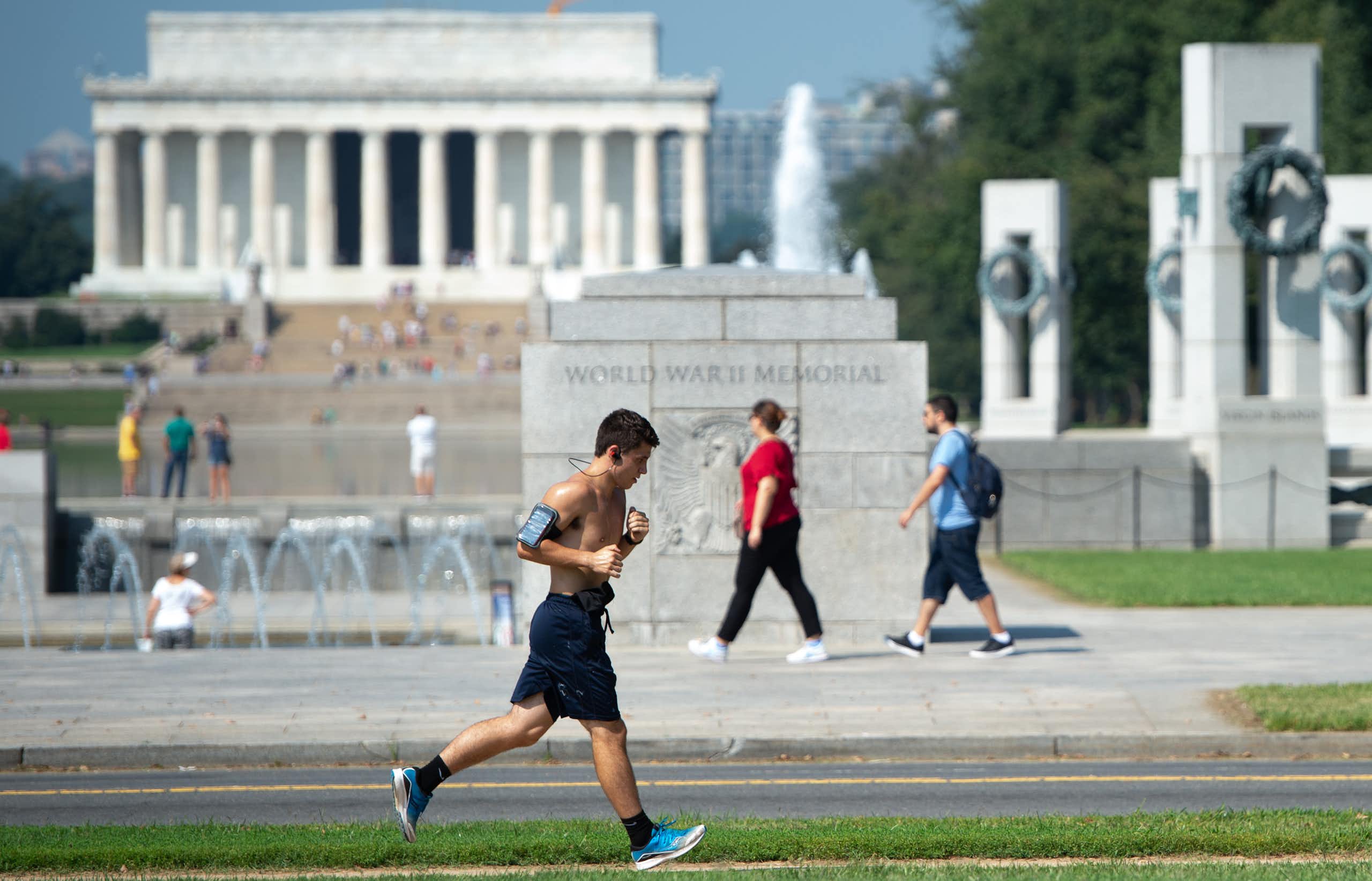 A man runs past the WWII Memorial on a hot day in Washington, D.C., with the Lincoln Memorial in the background