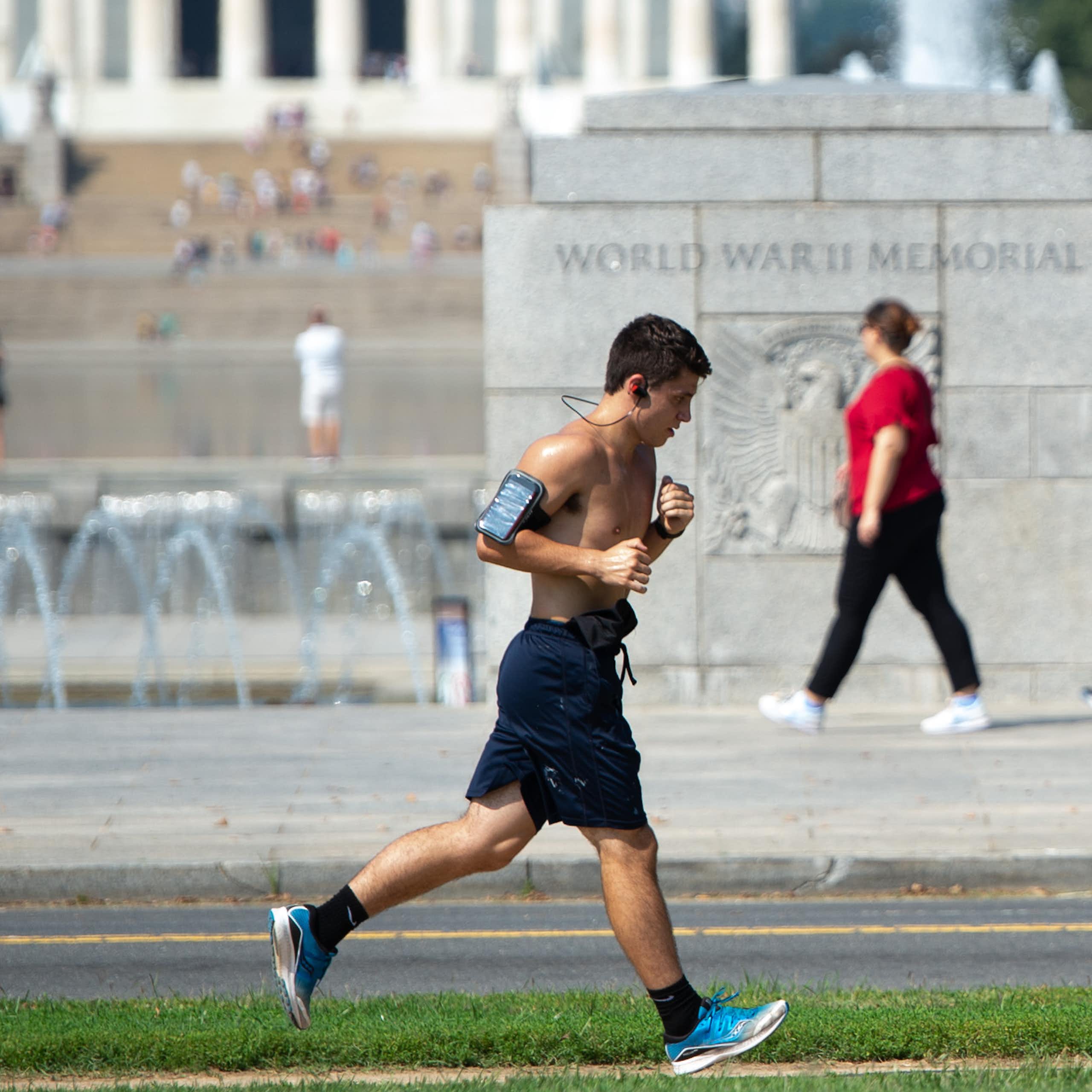 A man runs past the WWII Memorial on a hot day in Washington, D.C., with the Lincoln Memorial in the background
