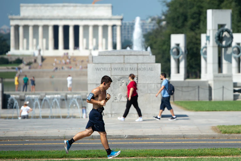 A man runs past the WWII Memorial on a hot day in Washington, D.C., with the Lincoln Memorial in the background