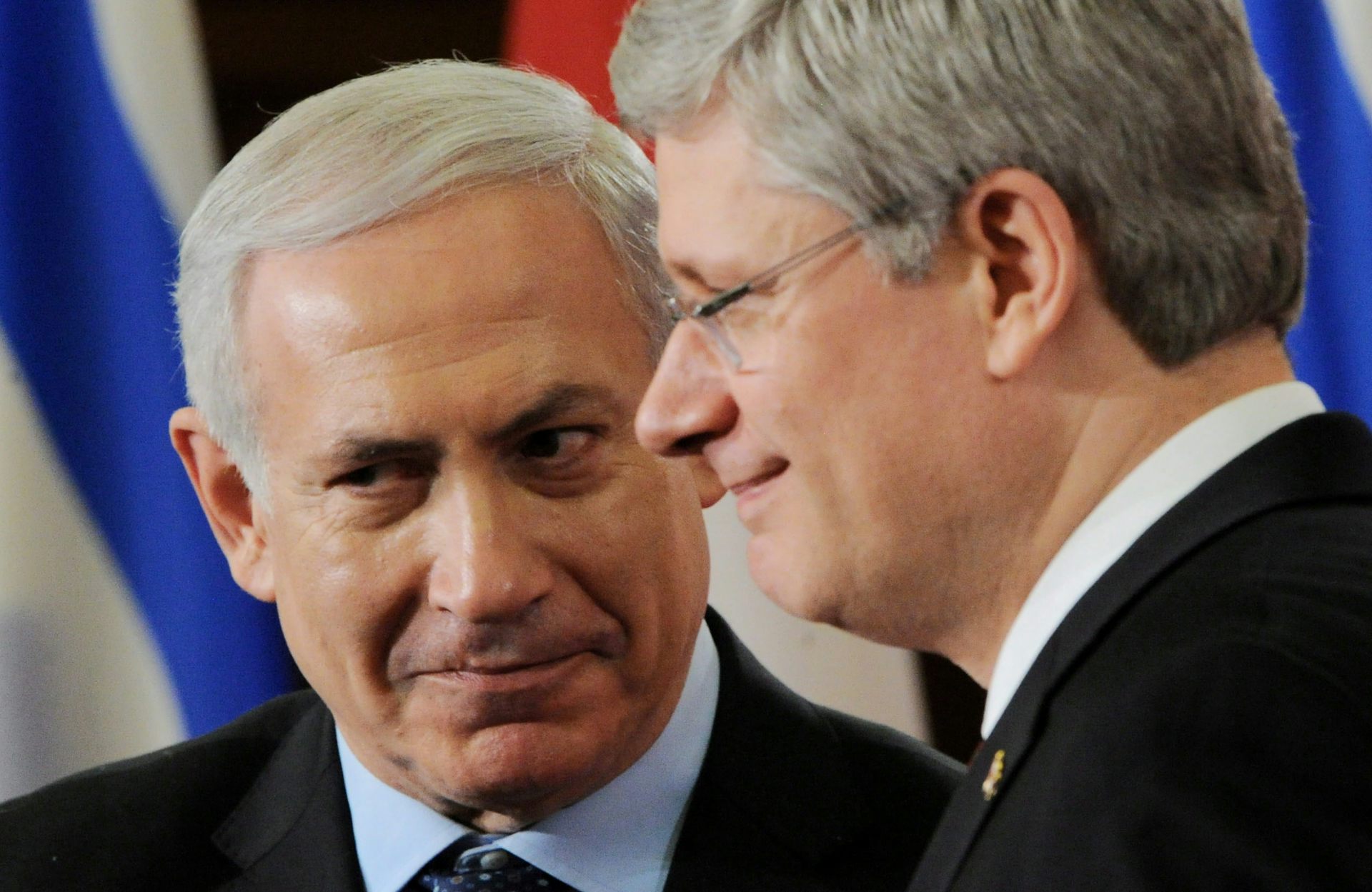 Two grey-haired men grin while standing close together.