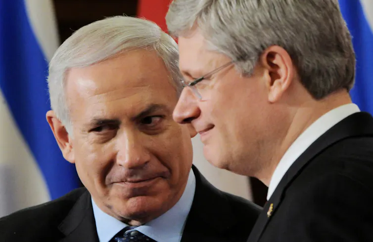 Two grey-haired men grin while standing close together.