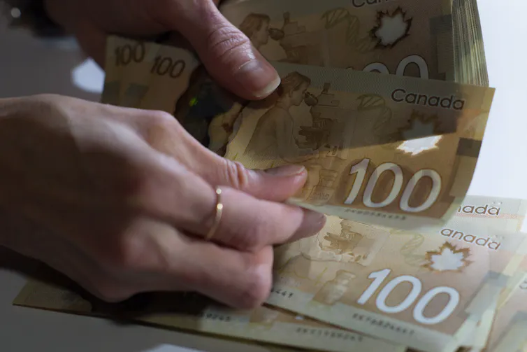 A pair of hands leafing through a pile of 100 dollar Canadian bills