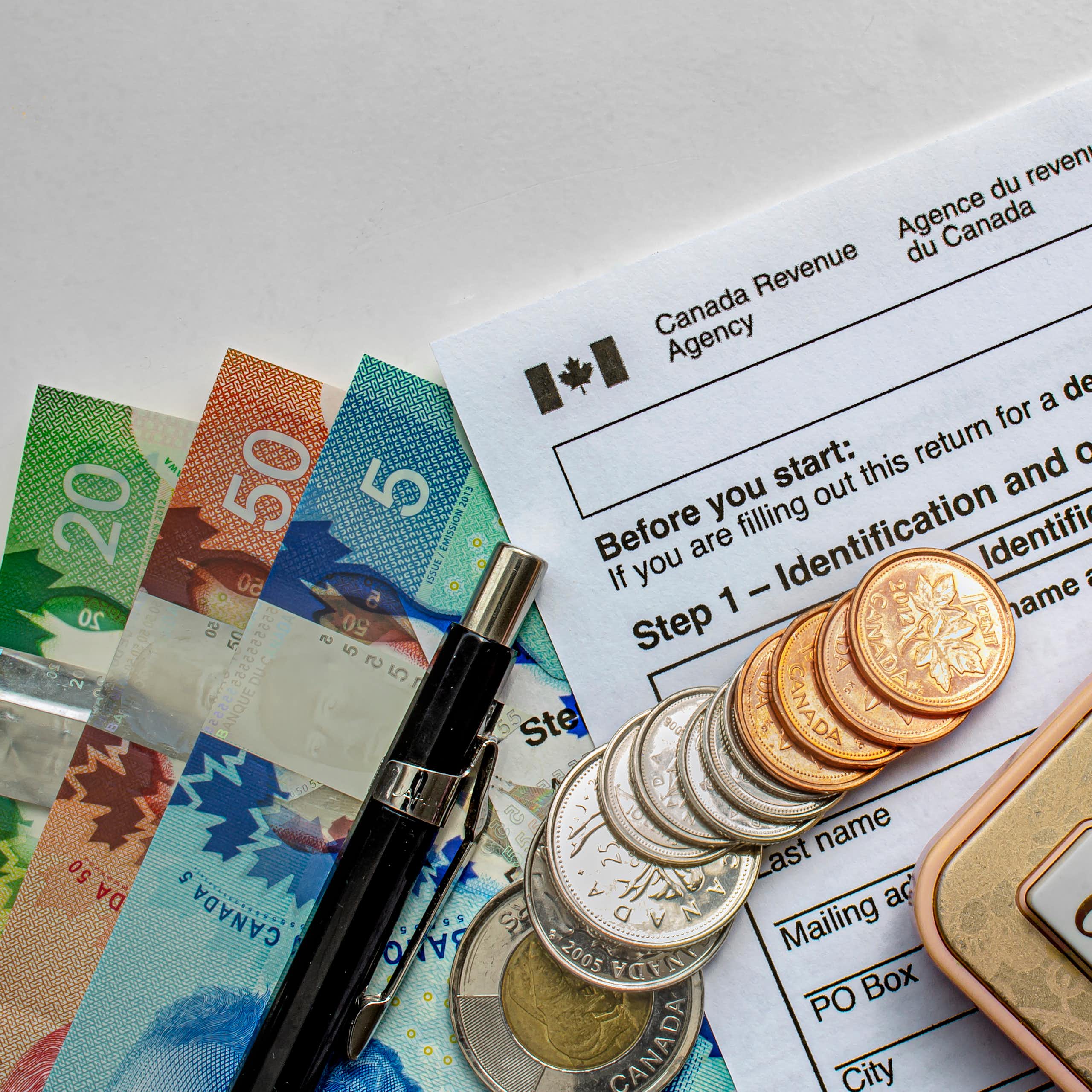 Canadian Tax Forms with coins, calculator, a pen and bills seen on a white table