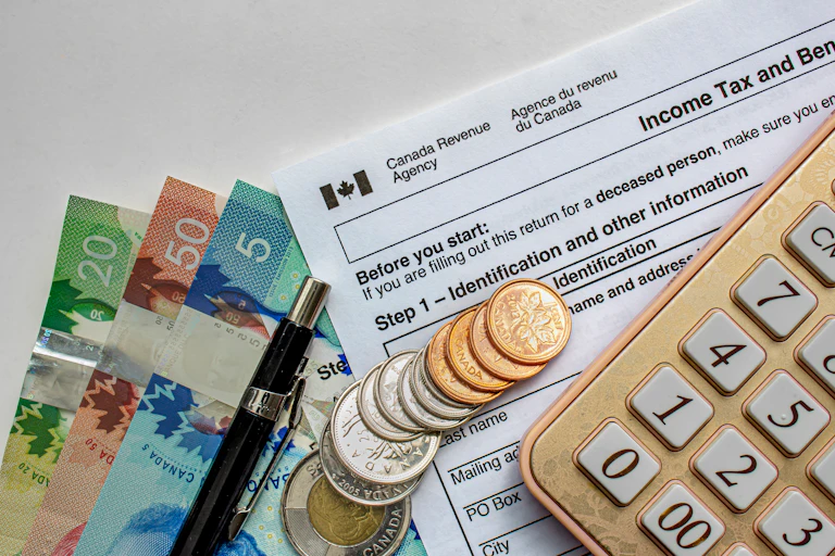 Canadian Tax Forms with coins, calculator, a pen and bills seen on a white table