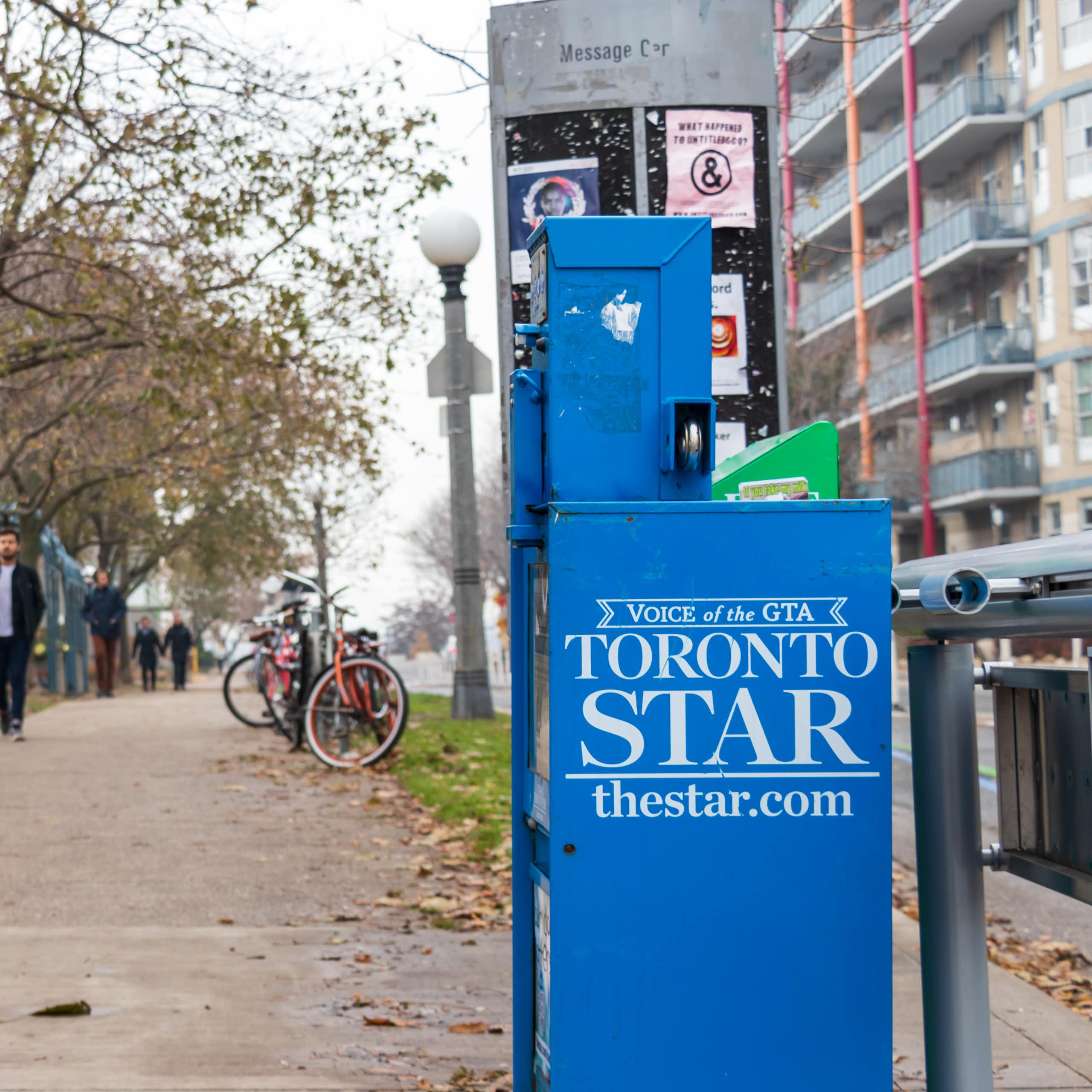 A newspaper vending machine with the Toronto Start logo on the side sits beside a city sidewalk