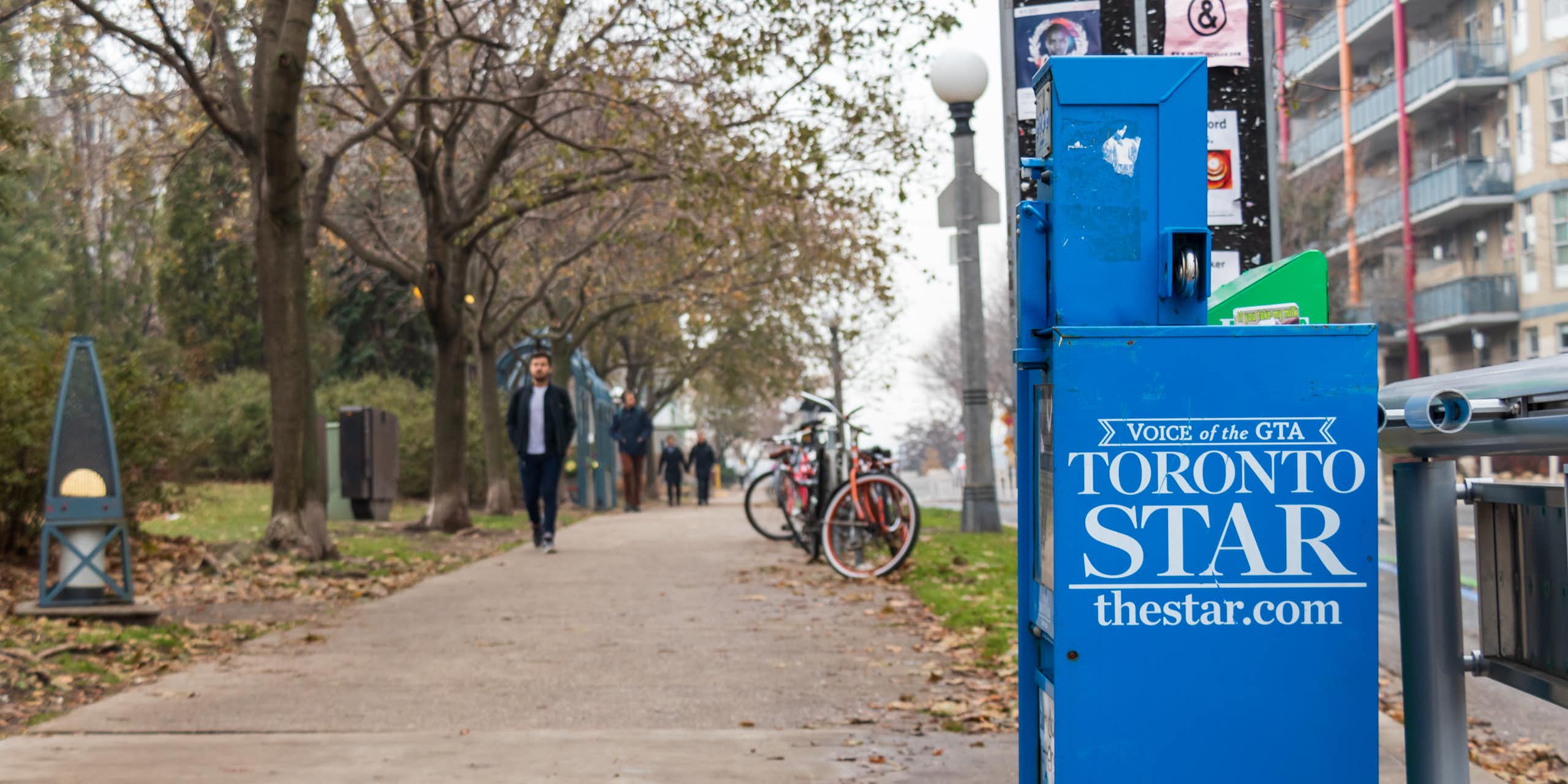 A newspaper vending machine with the Toronto Start logo on the side sits beside a city sidewalk