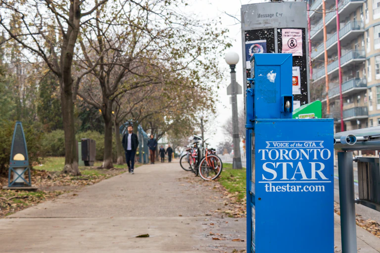 A newspaper vending machine with the Toronto Start logo on the side sits beside a city sidewalk