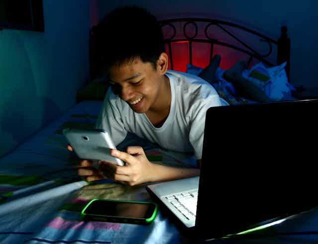 A young Indian teen in bedroom looking at smartphone and smiling.
