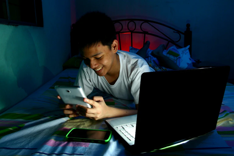 A young Indian teen in bedroom looking at smartphone and smiling.