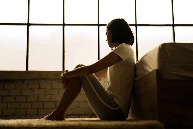 An Asian woman sits on the floor and looks away from the camera
