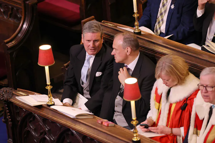 Keir Starmer and Ed Davey talking while sitting in pews next to two peers in ermine.