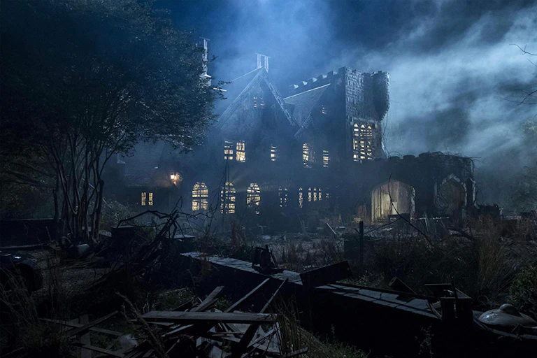 A scary old Gothic house from a horror film with lit but boarded windows.