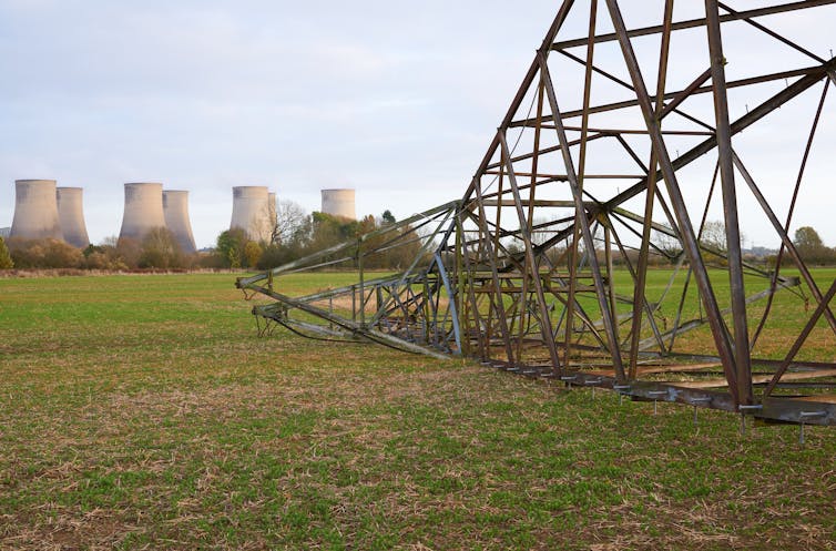 A fallen electricity pylon with power plant cooling towers in the distance.