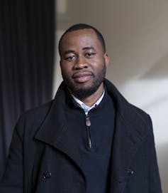 A man in a black coat smiles slightly as he poses for his portrait.