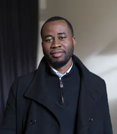 A man in a black coat smiles slightly as he poses for his portrait.