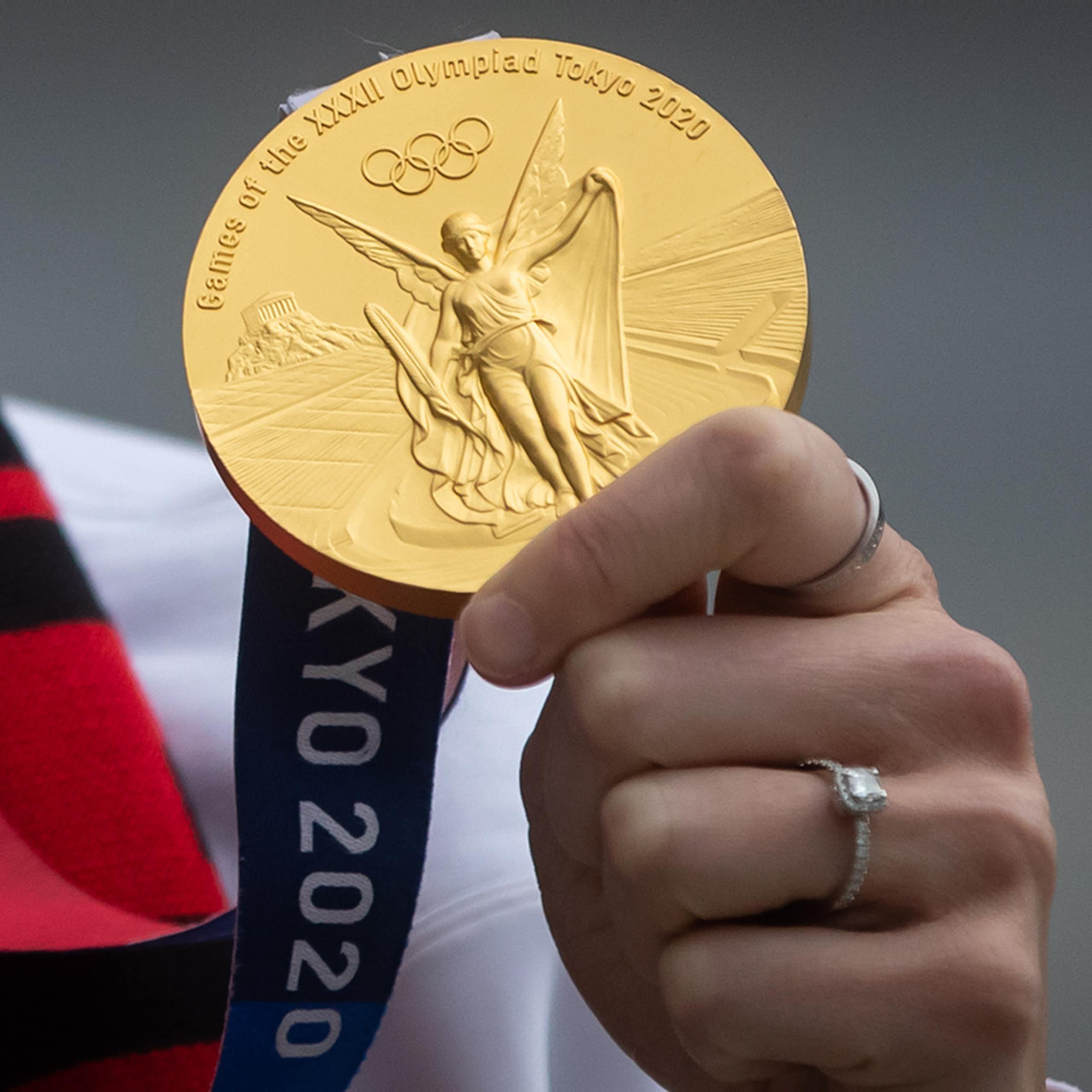 Close up of a hand holding up a gold medal from the Tokyo 2020 Olympics