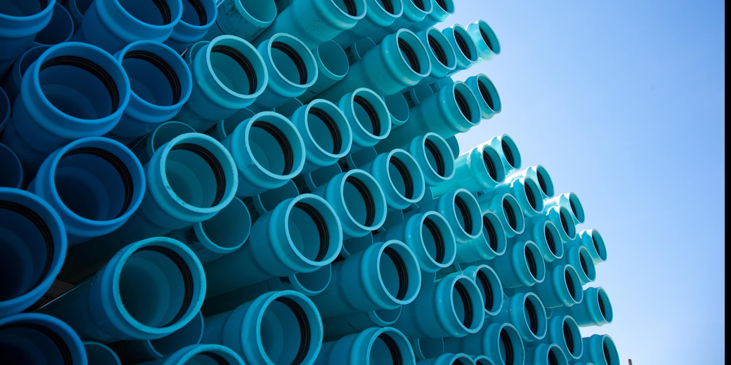 A stack of blue plastic water pipes under a blue sky