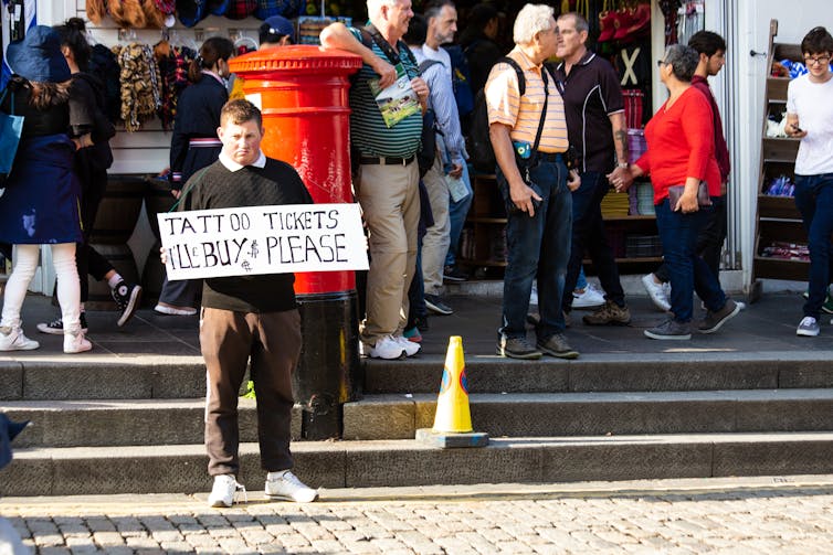 man on the street holding a sign saying he will buy tickets for the edinburgh tattoo