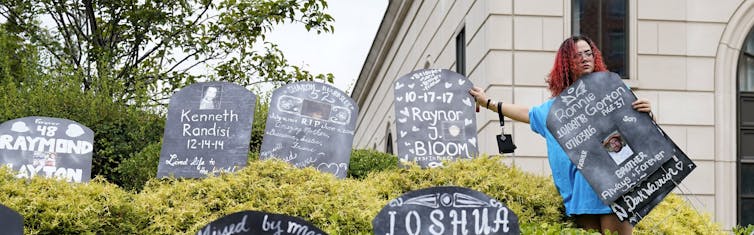 A woman stands among cardboard gravestones with the names of victims of opioid abuse.