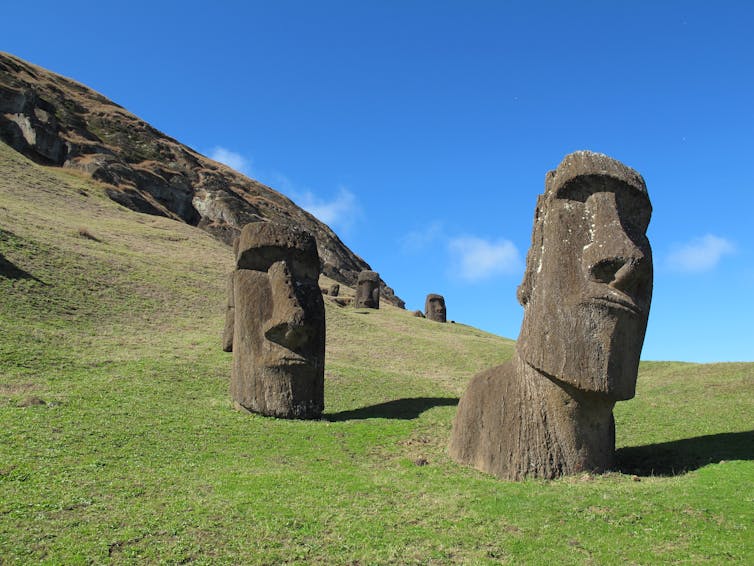 large stone carved heads sit on a grassy treeless aside