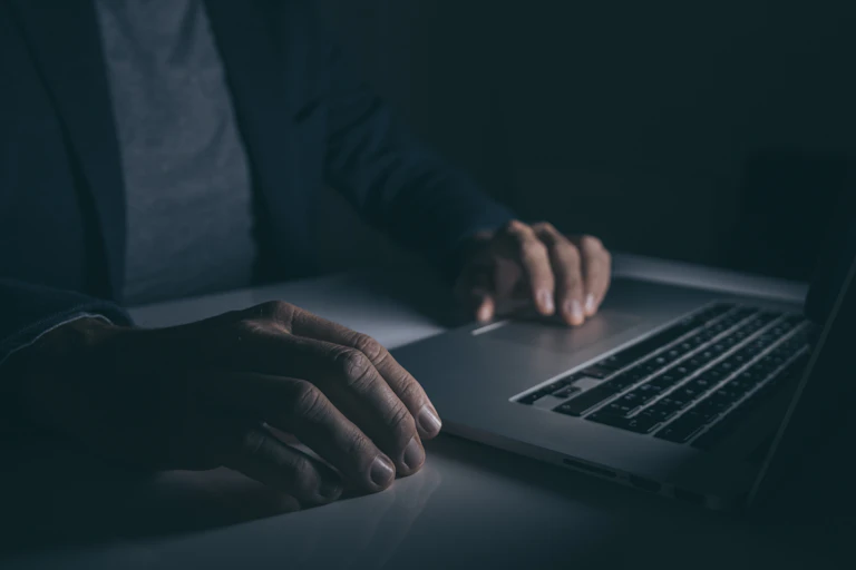 A dark room with some hands on a laptop keyboard