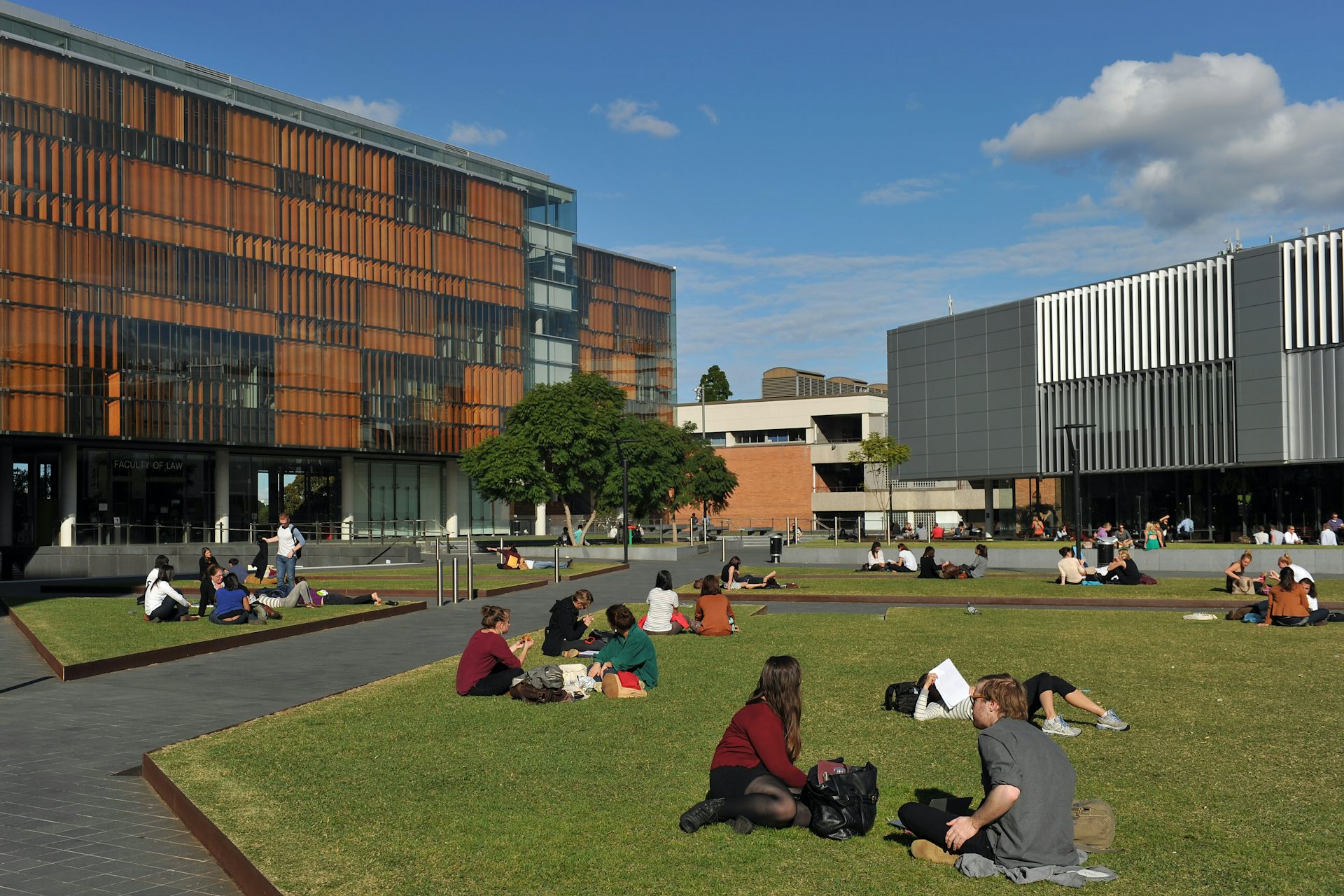 People sit on a lawn, surrounded by buildings.