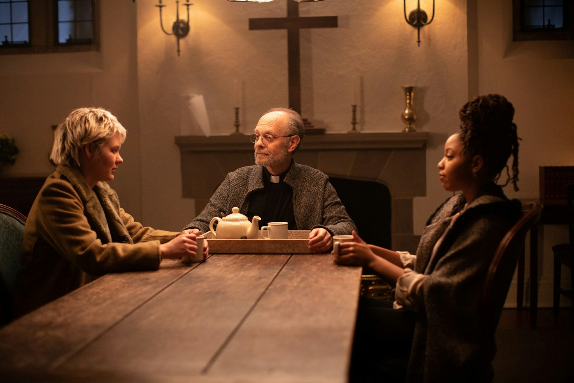 Two young women sitting round a table with an older priest.
