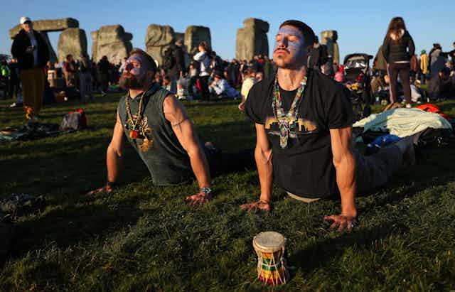 Two men perform yoga in front of Stonehenge.