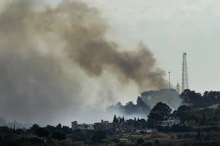 Smoke rises above buildings surrounded by trees