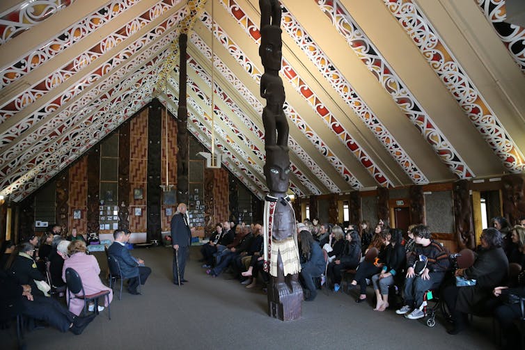 interior of whare nui (meeting house) with people listening to a speaker