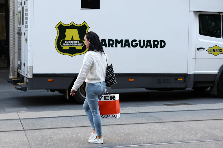 Woman crossing road carrying a shopping bag towards large truck parked at kerb
