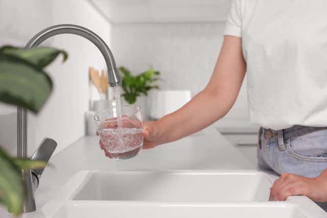 person fills water glass from tap in white kitchen