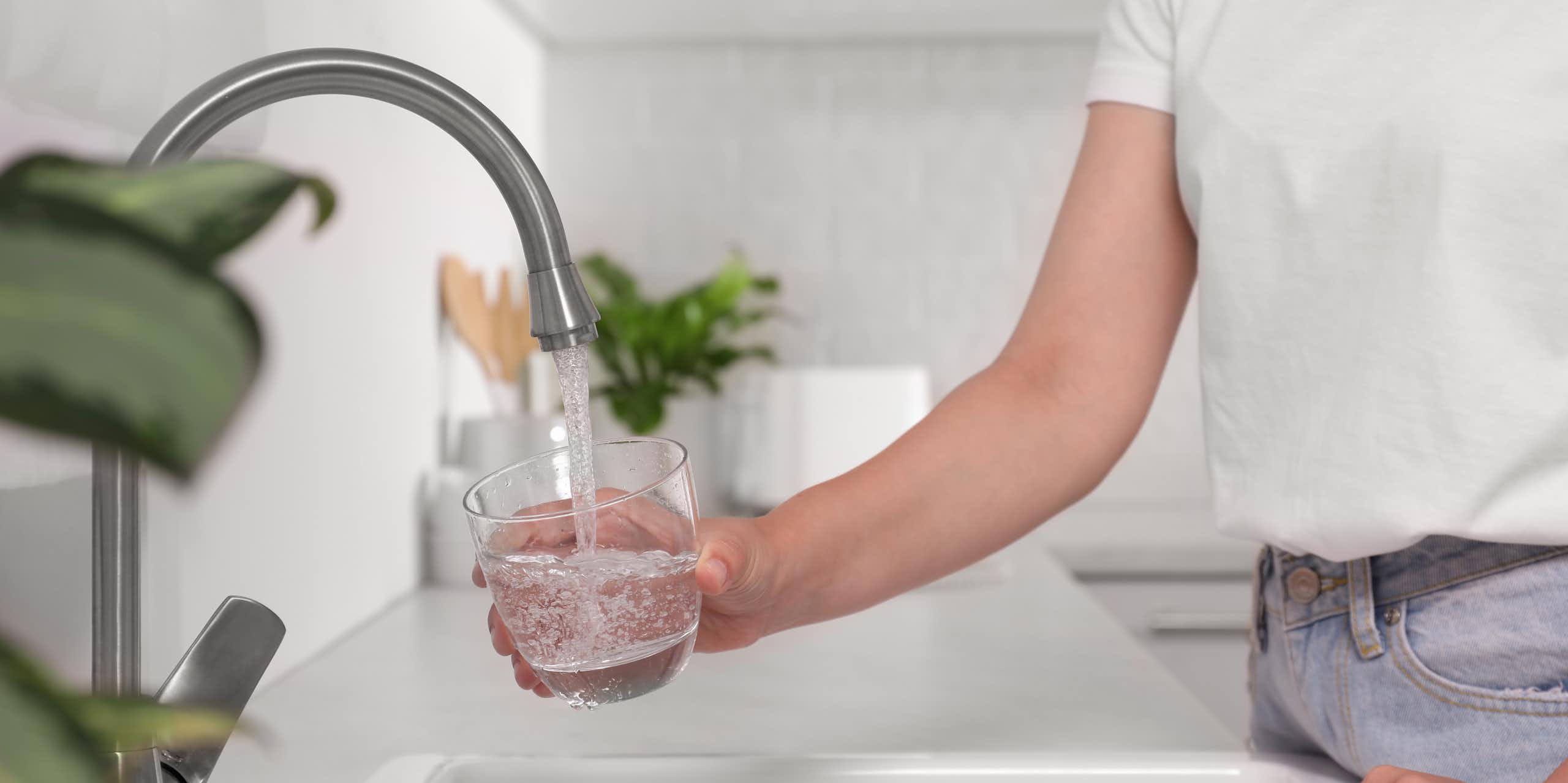 person fills water glass from tap in white kitchen