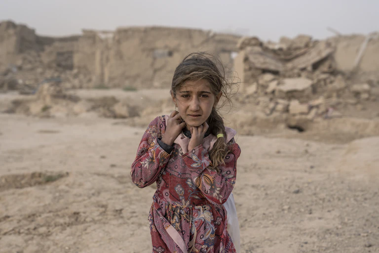 Girl stands in rubble-strewn desert landscape
